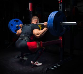 Professional athlete makes squats with a bar in the gym