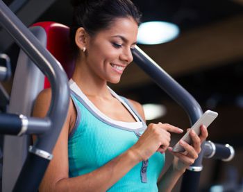 woman texting while sitting on machine in gym